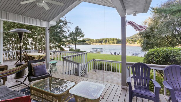 A covered outdoor deck with a table and chairs, overlooking a lake. - Lake front home (Hiawassee)