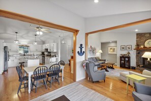 A spacious living area with a fireplace, a dining area with a large island, and a kitchen with white cabinets and a ceiling fan.