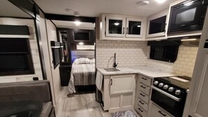 A compact kitchen with white cabinets, a microwave, a stove, and a sink.