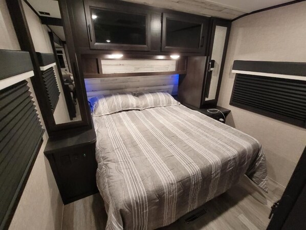 A compact RV bedroom with a bed, built-in TV, and overhead cabinets.
