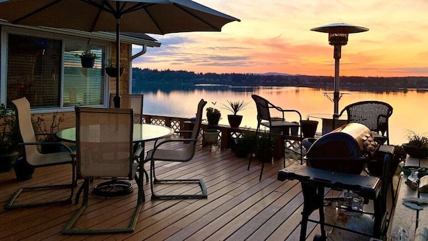 A deck with outdoor furniture, a grill, and a view of a lake at sunset.