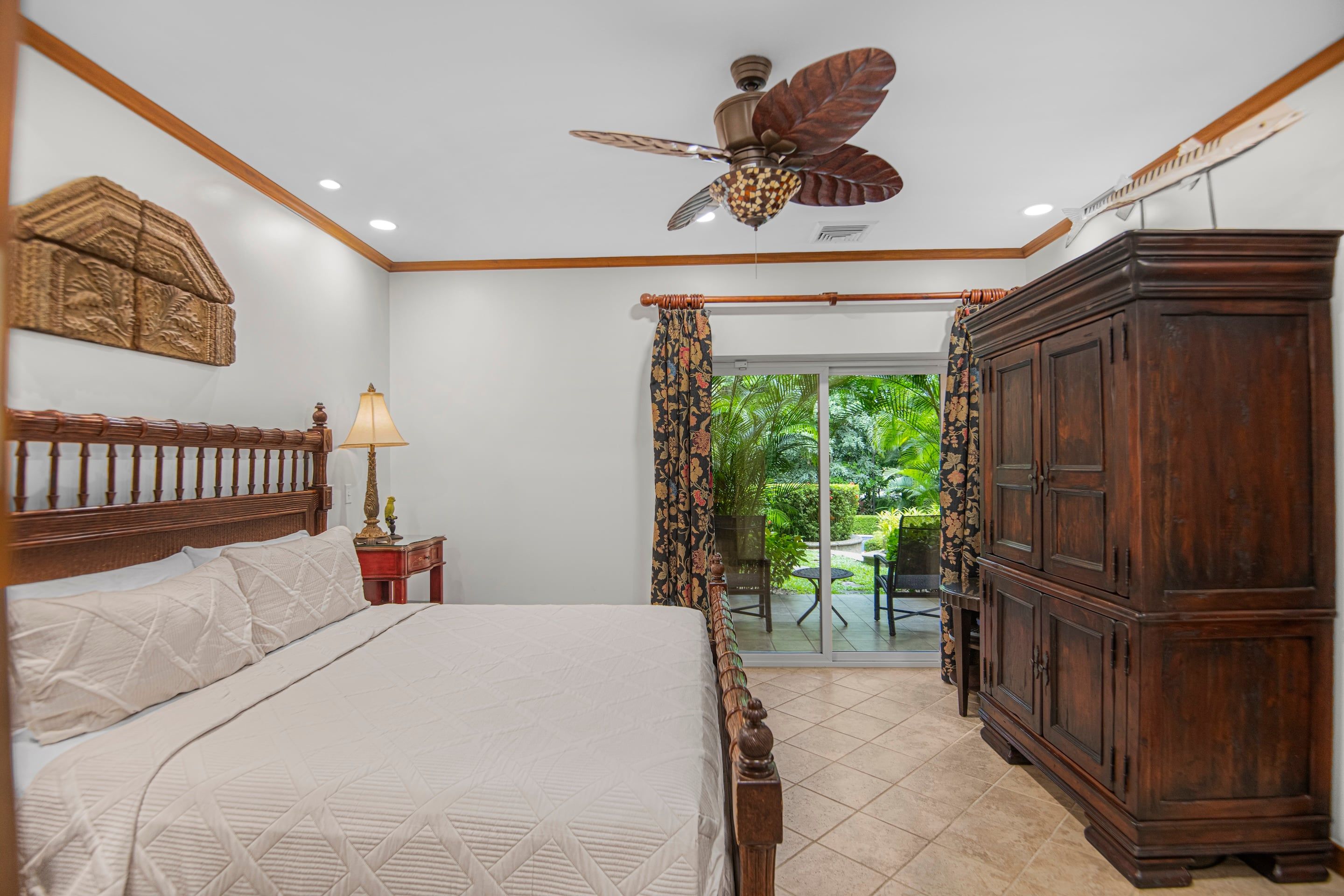 A bedroom with a bed, a nightstand, a lamp, a wooden wardrobe, and a ceiling fan.