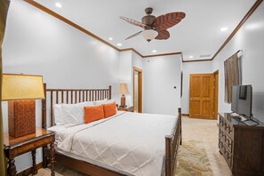 A bedroom with a bed, wooden headboard, bedside lamps, a ceiling fan, a wardrobe, and a television.
