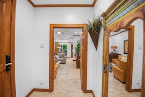A hallway with a wooden door, a ceiling fan, and a mirror reflecting a room with a sofa and a lamp.