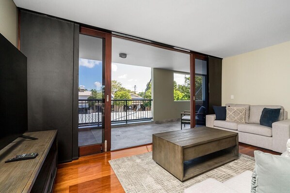 Relax in this serene living space with a large balcony offering views of the surrounding area, a comfortable sofa, and a functional TV stand.