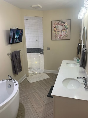 Casa de banho moderna com banheira, duas pias, zona de duche e televisão na parede.