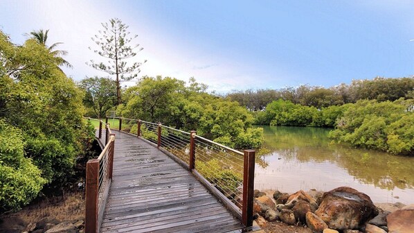 A wooden bridge over a calm river, surrounded by lush greenery and trees. - Villa 25 Coral Cove Resort (CORAL COVE)