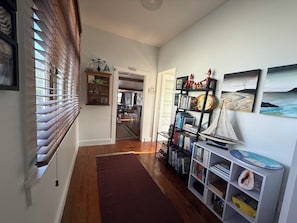 A hallway with wooden flooring, a bookshelf with books and decorative items, a rug, and a door leading to another room.