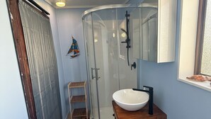 Un baño con cabina de ducha de vidrio, tocador de madera y un estante pequeño.