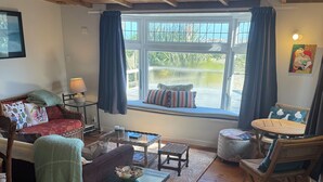 Una sala acogedora con techo de madera, un sofá con cojines estampados, una mesita, una silla y vistas a través de una ventana.