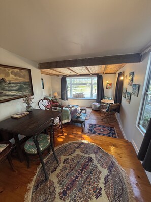 Un salon chaleureux avec une table à manger en bois, des sièges confortables, une grande fenêtre avec des rideaux et un tableau accroché au mur.