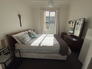 A bedroom with a bed, a dresser, a mirror, a window with curtains, and a lamp.
