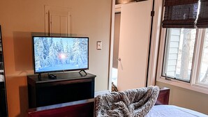 Un dormitorio con cama, televisor sobre un mueble, una puerta y una ventana con persianas.