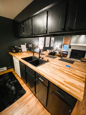 A modern kitchen with black cabinets, a wooden countertop, a sink, and a dishwasher.
