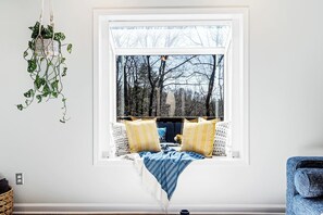 A room with a window seat, a hanging plant, and a blue chair.
