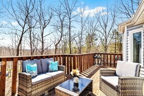 A deck with wicker furniture, a glass table, and a view of leafless trees.