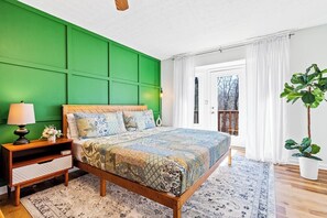Een slaapkamer met een groene accentmuur, een houten bedframe, een nachtkastje met een lamp en uitzicht op het omliggende landschap door een raam.