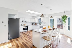 Una cocina moderna con armarios blancos, una isla central con taburetes altos y un refrigerador negro, con iluminación colgante.