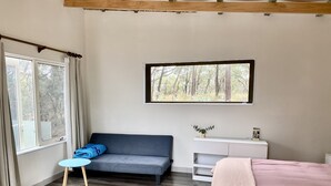 A room with a grey sofa, a small table with a blue cloth, a white cabinet, and a bed with a pink blanket.