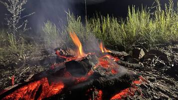 Un feu de camp avec des braises et des flammes incandescentes, entouré d’herbe et de rochers.