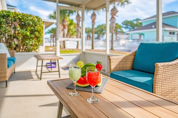 A covered outdoor seating area with wicker furniture and a table with drinks.
