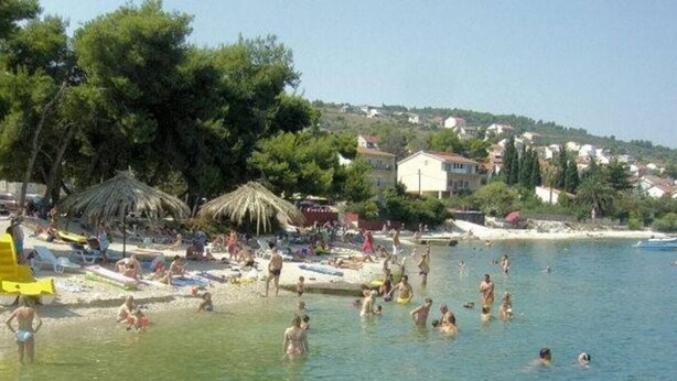A beach with people swimming and sunbathing, surrounded by trees and houses. - Beautiful Apartment with Sea View, Trogir, Croatia (Mastrinka)