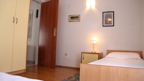 Une chambre avec une armoire en bois, une table de chevet avec une lampe, un lit et une porte donnant sur une autre pièce.