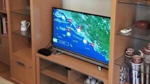 A living room with a television on a wooden stand, surrounded by shelves with various items. - Beautiful Apartment with Sea View, Trogir, Croatia (Mastrinka)