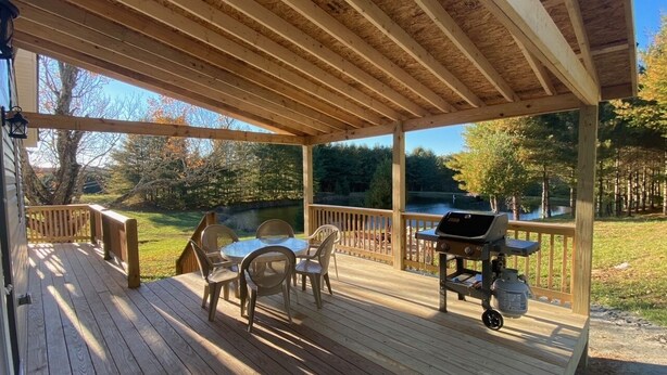 Une terrasse en bois avec des meubles d’extérieur, un barbecue et une vue sur un lac.