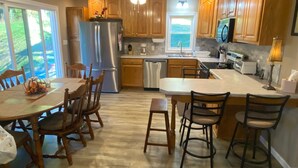 Une cuisine moderne avec des meubles en bois, un réfrigérateur en acier inoxydable, un coin repas avec des chaises en bois et un grand îlot central doté de tabourets de bar.