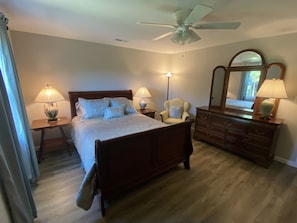 Un dormitorio con cama, cómoda, silla, lámpara, ventilador de techo y espejo.