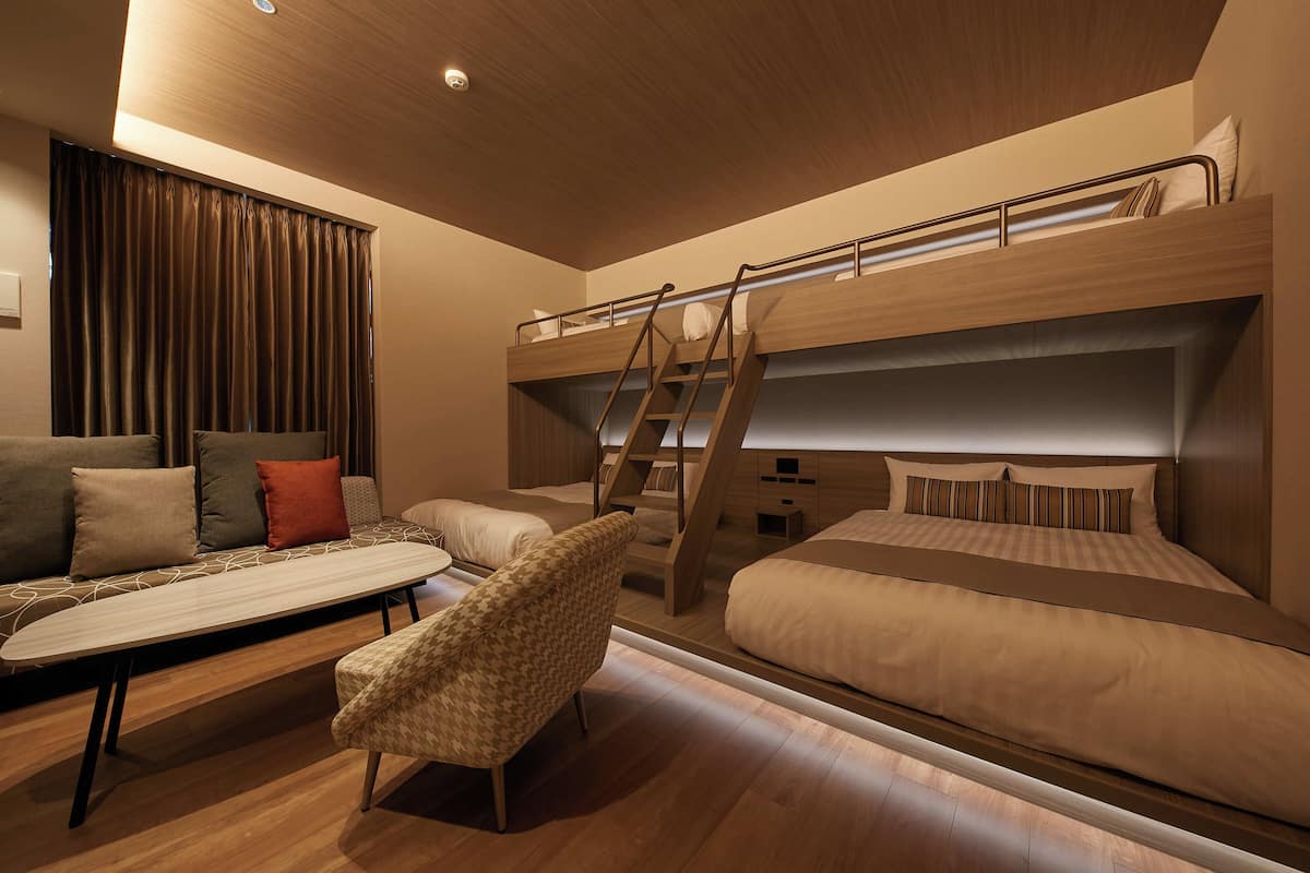 A modern bedroom with a bunk bed, a sofa, a chair, and a desk.