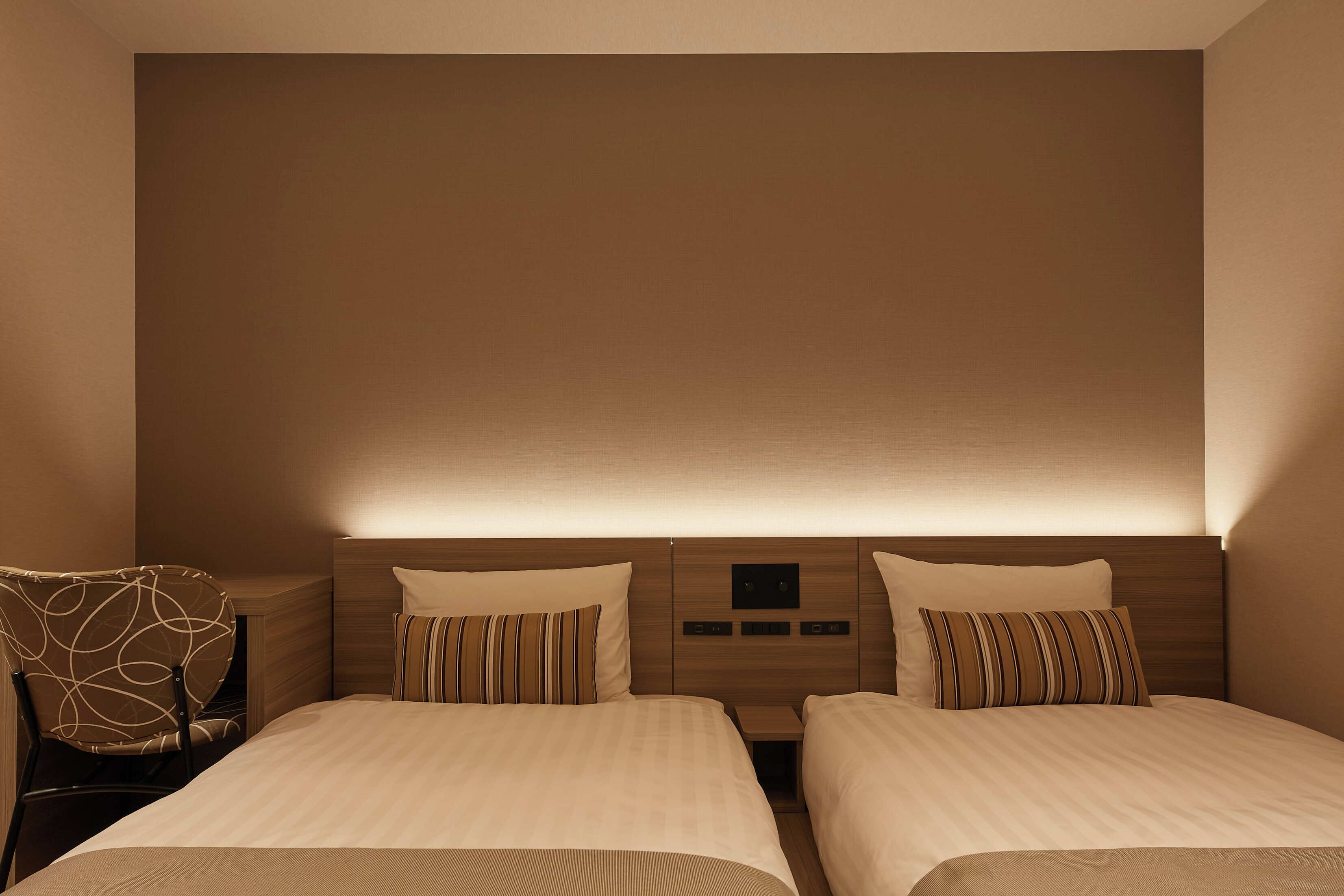 Une chambre d’hôtel avec deux lits, une chaise et une tête de lit dotée d’un panneau de commande.