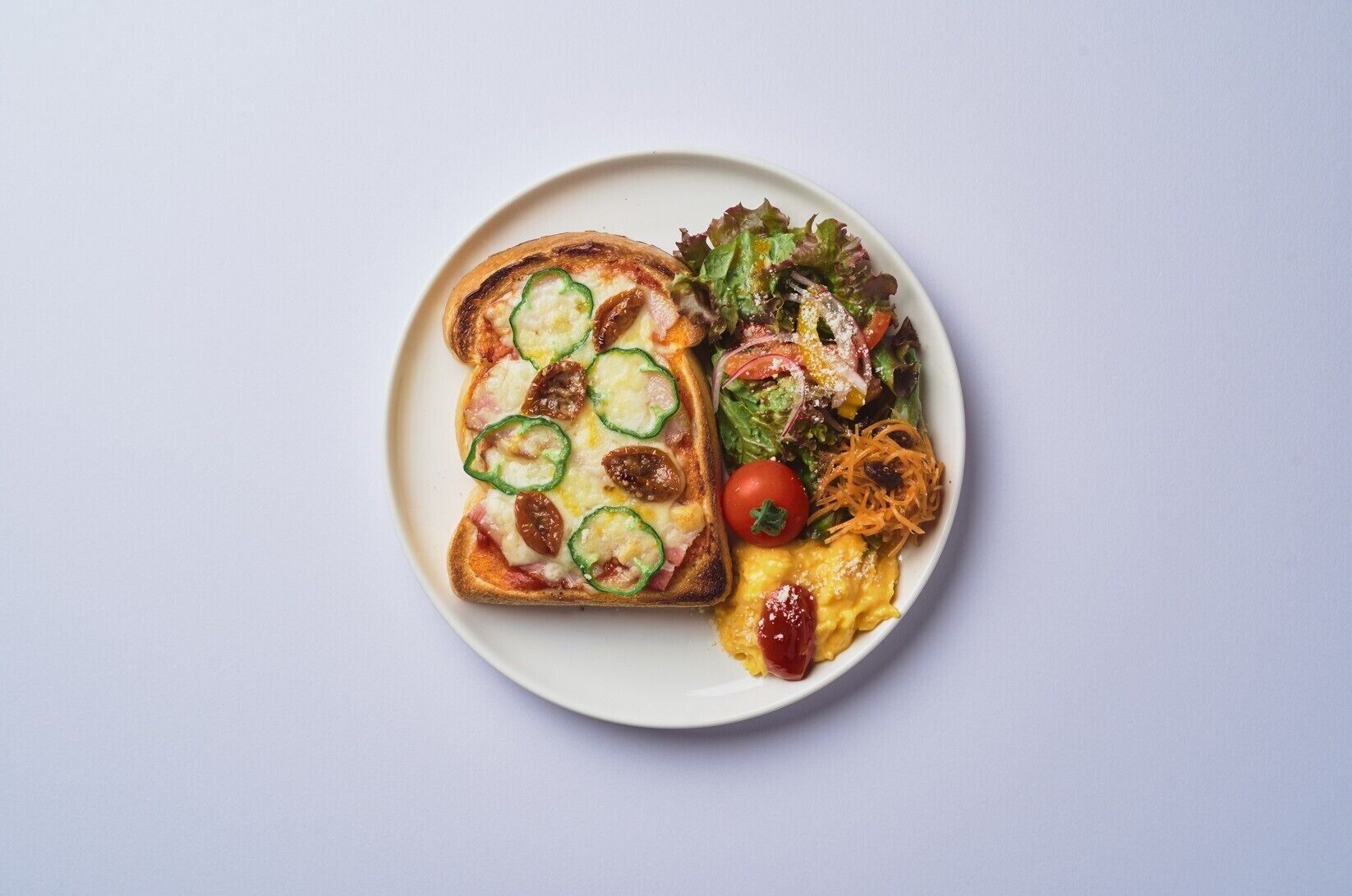 A plate with a slice of toast topped with cheese and vegetables, a salad with mixed greens and cherry tomatoes, and a serving of scrambled eggs.