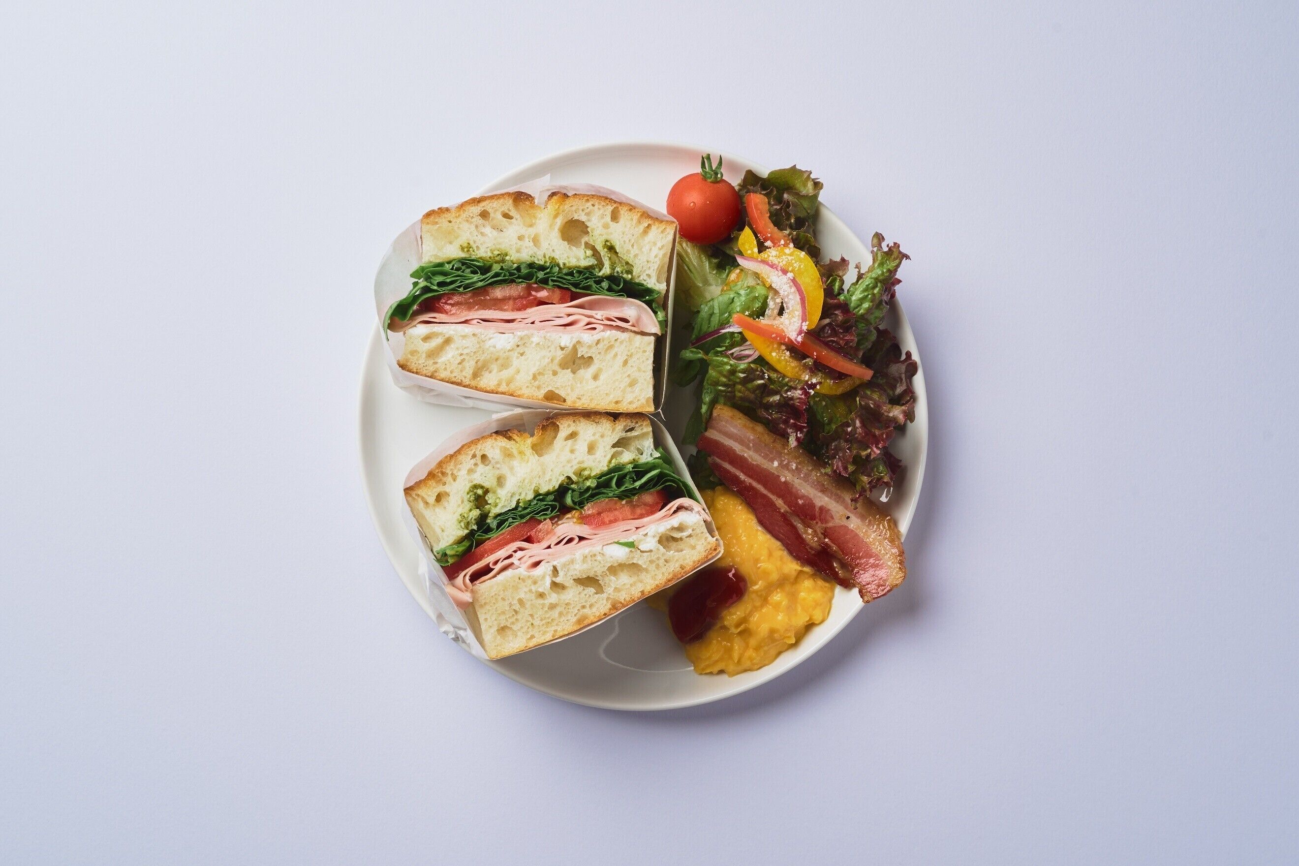 Une assiette avec un sandwich, une salade et des œufs brouillés.