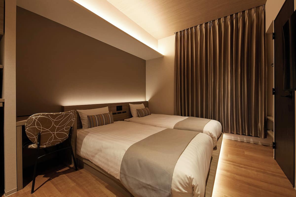 A hotel room with two beds, a chair, and a large window with curtains.