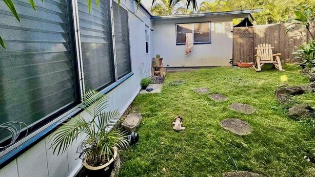 A backyard with a small house, a wooden chair, and a potted plant.