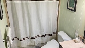 A bathroom with a white shower curtain, a toilet, a sink, and a trash can.