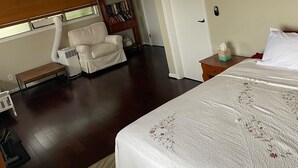 A bedroom with a bed, a ceiling fan, a chair, a bookshelf, and a window with blinds.
