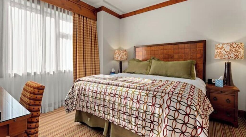 A hotel room with a large bed, two bedside tables, a chair, and a desk.