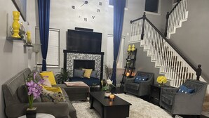 Ein Wohnzimmer mit Sofa, Sesseln, Couchtisch, Kamin, Treppe und Dekorationselementen.
