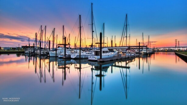 Marina con varios veleros amarrados en aguas tranquilas que reflejan el atardecer.
