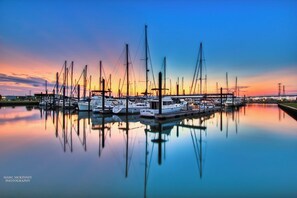 A marina with multiple sailboats docked at calm water reflecting the sunset.