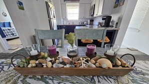 Una mesa de comedor con un centro de conchas marinas y velas, rodeada de sillas.