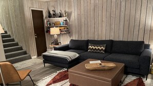 A modern living room with a dark grey sofa, a wooden coffee table, and a patterned rug.