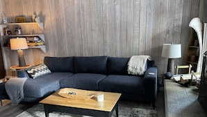 A modern living room with a dark blue sofa, a wooden coffee table, and a patterned rug.