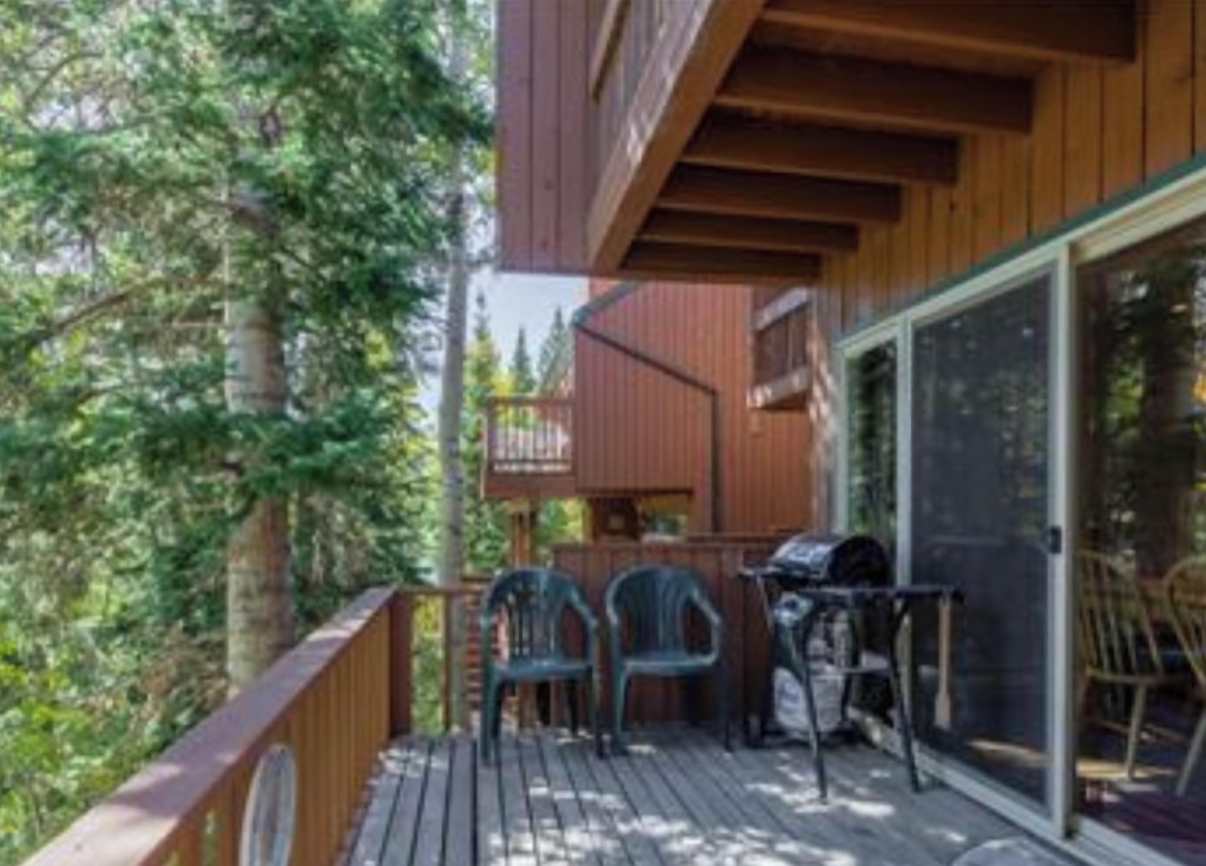 A back deck with a wooden railing, a barbecue grill, and two chairs.