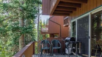 A back deck with a wooden railing, a barbecue grill, and two chairs.