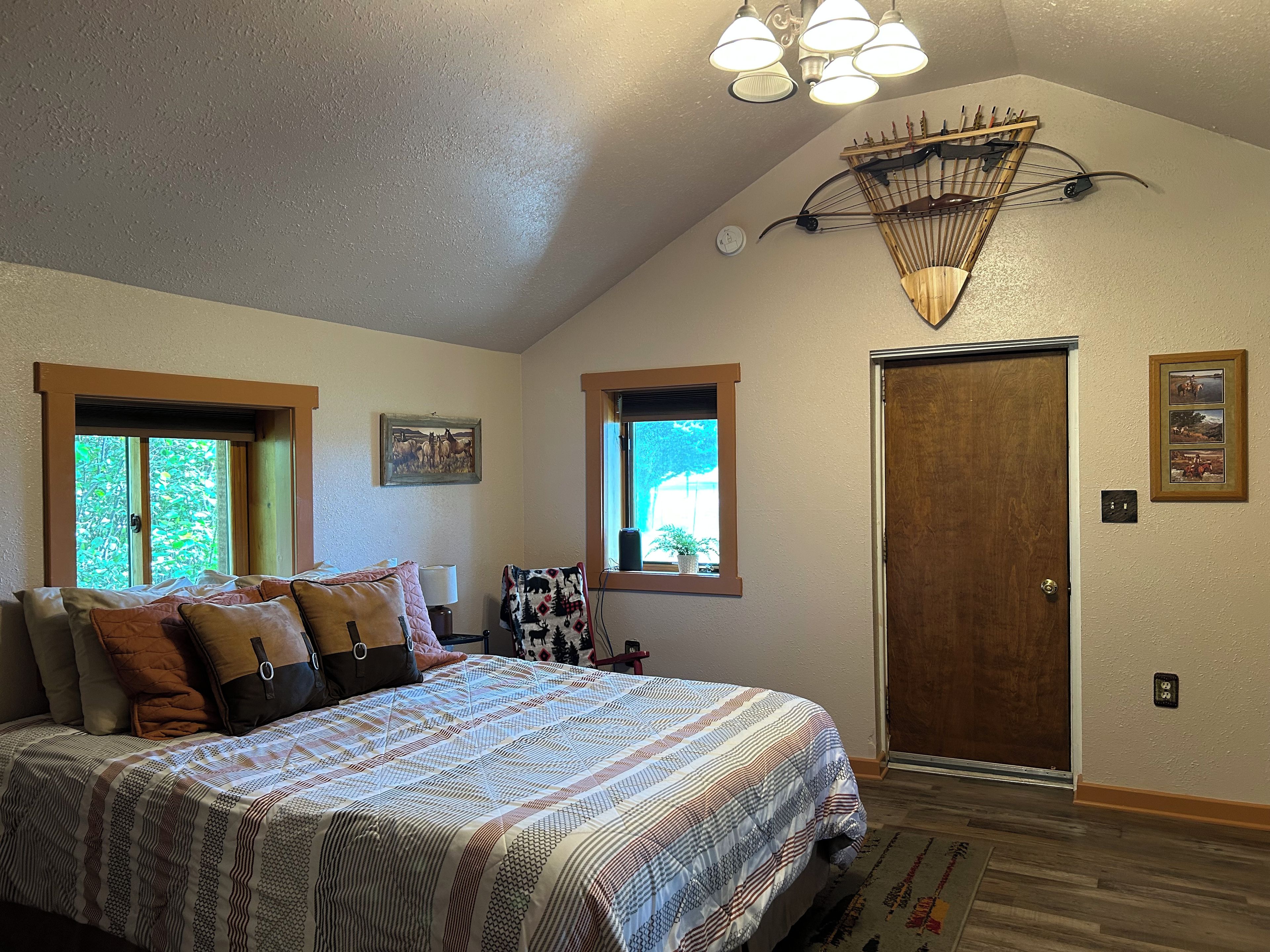 A bedroom with a large bed, two windows, a door, and a ceiling light fixture.