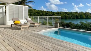 A wooden deck with two lounge chairs and a pool. - Villa NALA seaside pool standing, relaxation facing the lagoon feet in the water  (LE ROBERT)